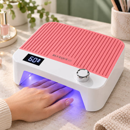 Lampă UV LED reîncărcabilă BQ L17 roz în funcțiune pe masa de manichiură, cu mâna poziționată în interior, lumină violetă, afișaj digital și decor de salon în tonuri naturale.