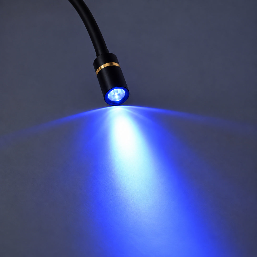 Detaliu al capului cilindric negru al lămpii UV LED pentru gene, cu inel auriu și lumină albastră proiectată pe suprafața de lucru.