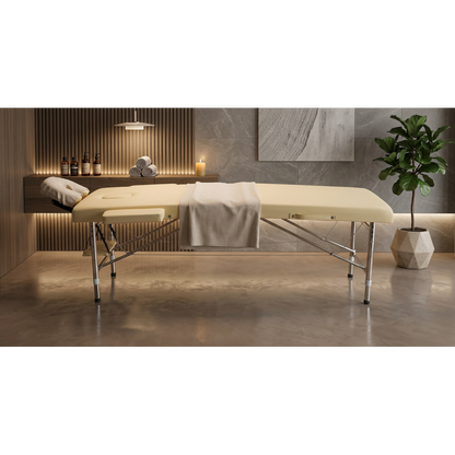 Masa Gene / Pat Masaj Portabil din Aluminiu Premium Gold, de culoare bej, asezat intr-un cadru modern de salon de infrumusetare, cu o planta decorativa si perete de accent in spate.