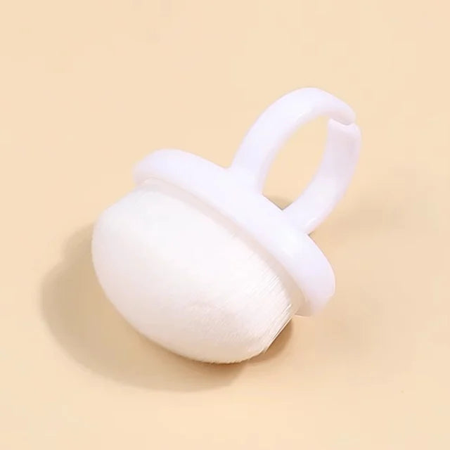 Perie tip inel pentru indepartarea prafului de pilire de pe unghii, fotografiata de sus pe un fundal minimalist bej-crem.