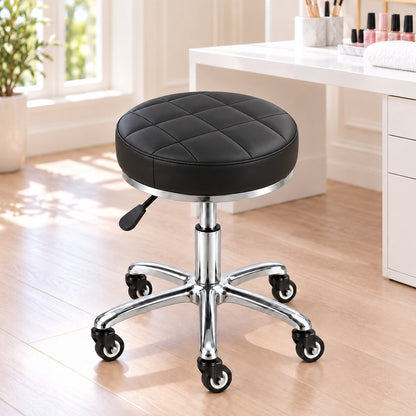 Scaun cosmetică DIVA Platinum cu șezut negru capitonat și bază cromată cu roți, așezat lângă o masă de manichiură într-un salon luminos.