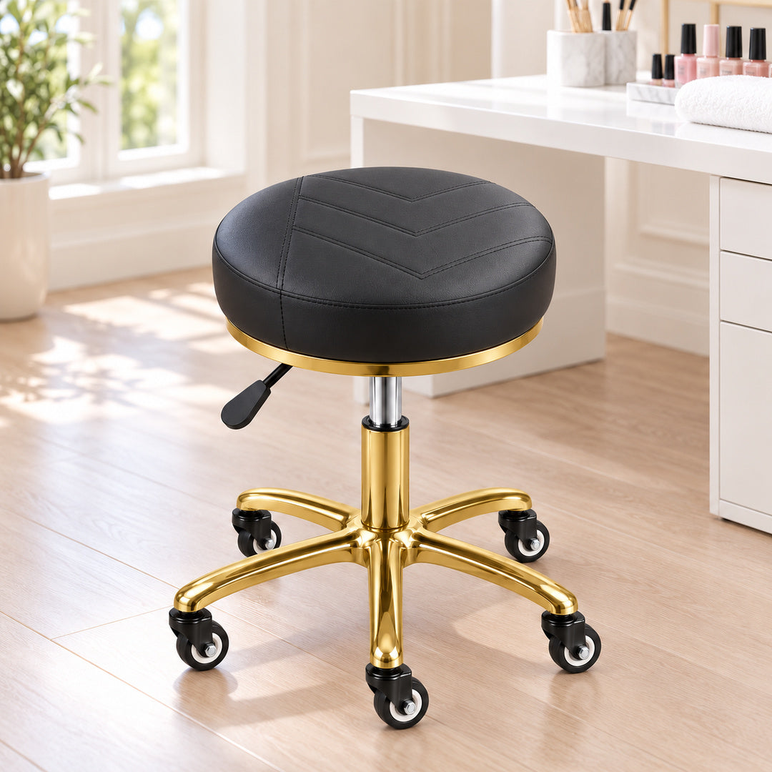 Scaun cosmetică DIVA Gold cu șezut negru și bază aurie, poziționat lângă o masă de manichiură într-un salon luminos.